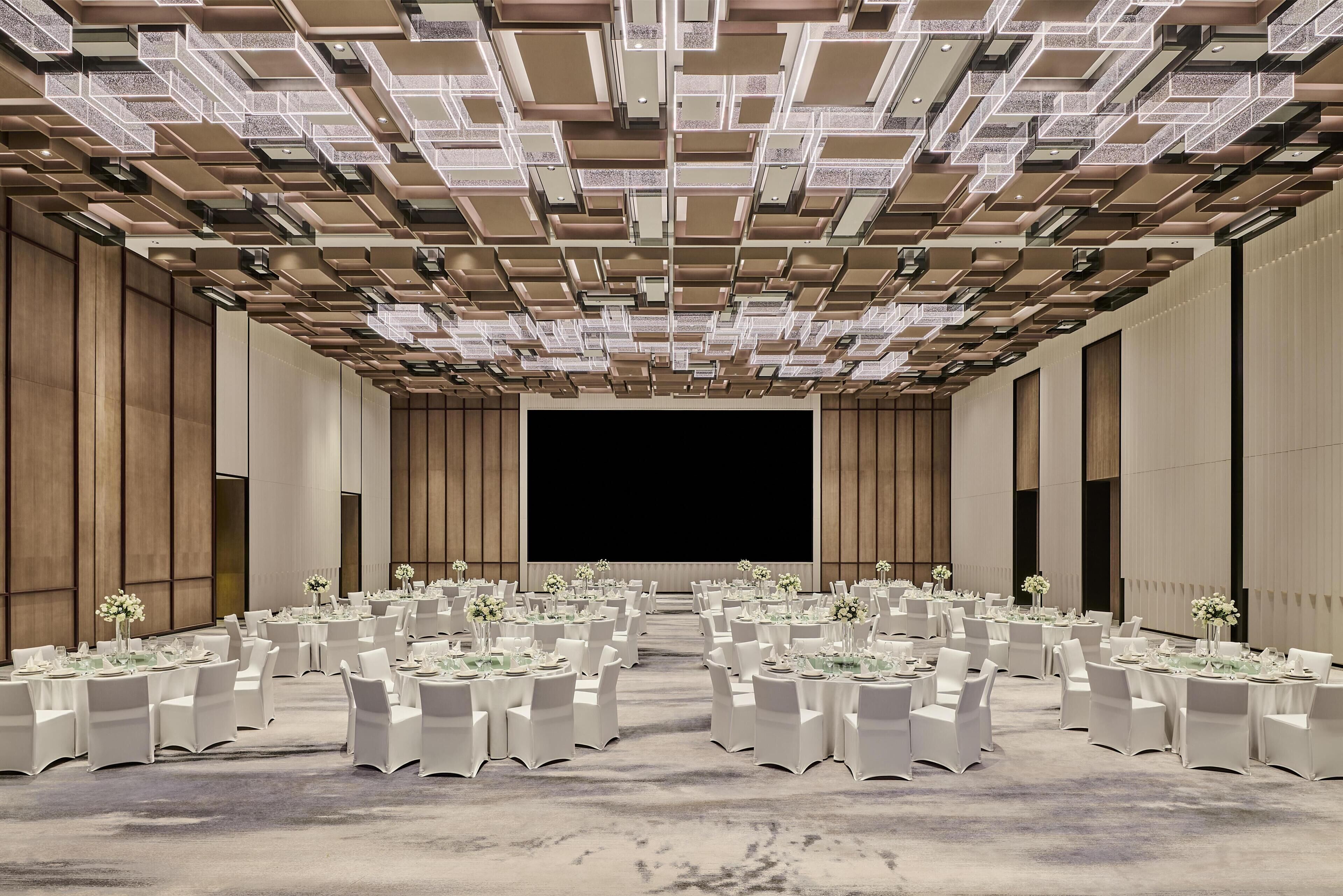 A large conference room with multiple round tables, white chairs, and a stage at the front.