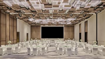 A large conference room with multiple round tables, white chairs, and a stage at the front.
