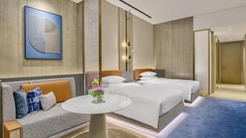 A hotel room with a sofa, a round table with a vase, two beds, and a large abstract painting on the wall.