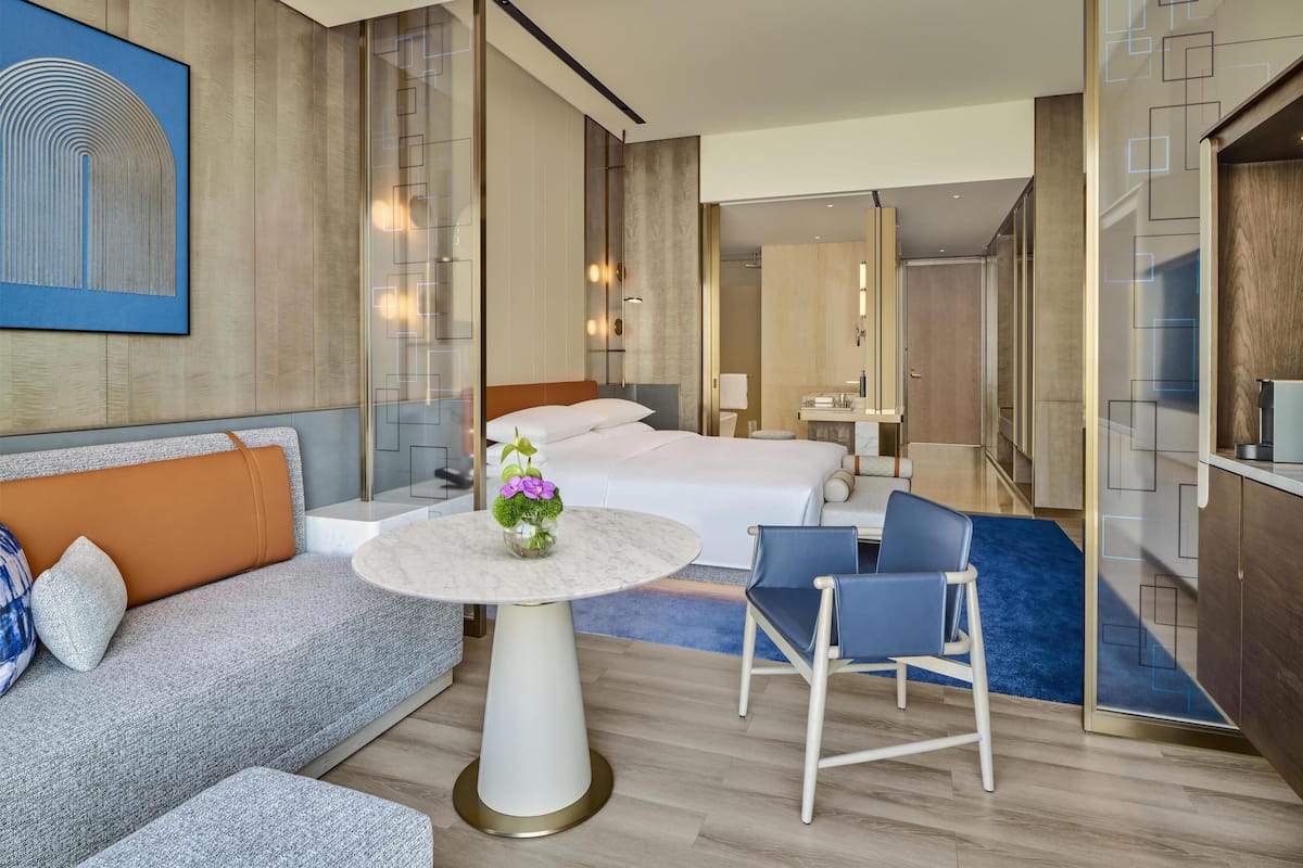 A modern hotel room with a bed, sofa, round table, and a chair.