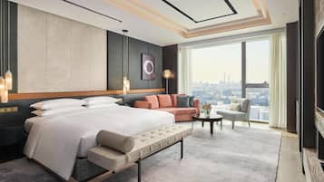 A modern hotel room with a large bed, a sofa, a small table, and a city view.
