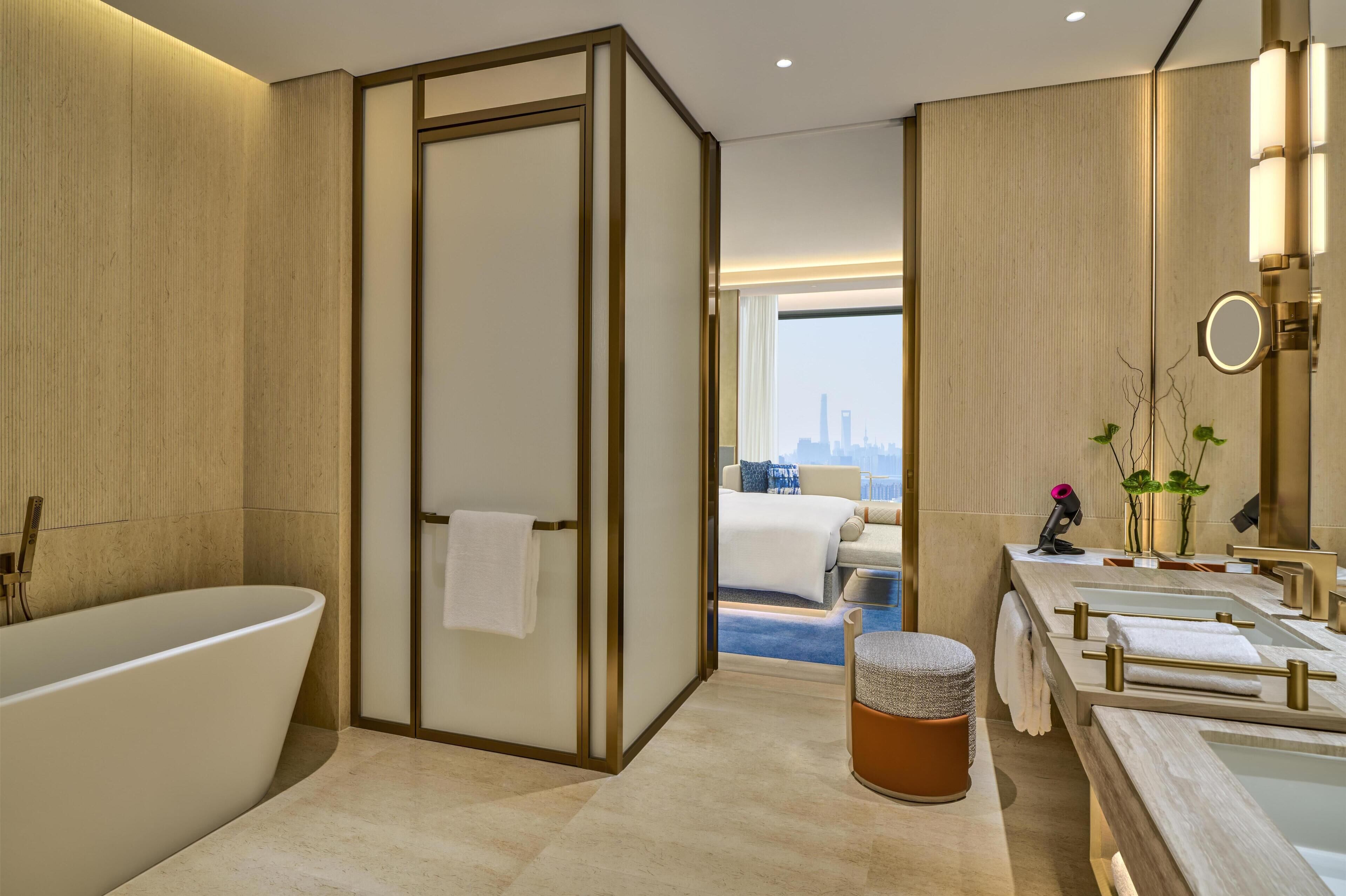 Un baño moderno con una bañera independiente, una ducha a ras de suelo, un tocador con espejo y vistas a la ciudad.