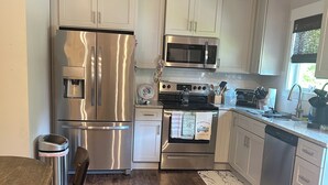 A modern kitchen with stainless steel appliances, white cabinetry, and a wooden floor.