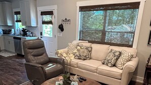A living room with a beige sofa, a brown leather chair, a round wooden coffee table, and a patterned rug.