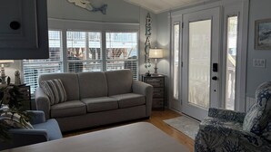 Una sala de estar con un sofá gris, un sillón estampado, una mesa de centro blanca y un ventilador de techo.