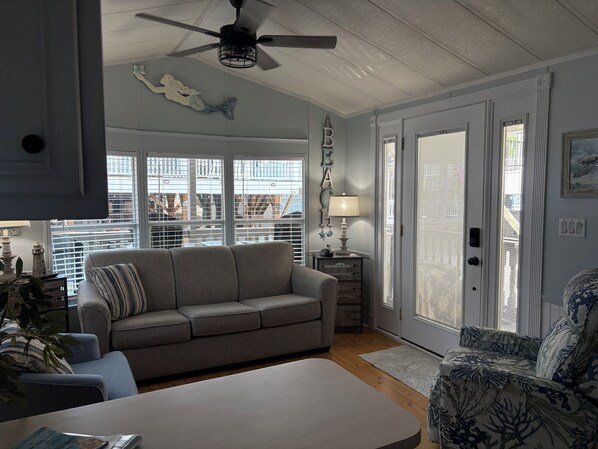 A living room with a gray sofa, a patterned armchair, a white coffee table, and a ceiling fan.