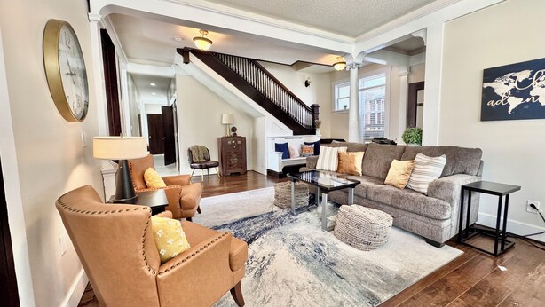 A spacious living room with a brown leather armchair, a grey sofa, and a coffee table. A staircase leads to an upper level.