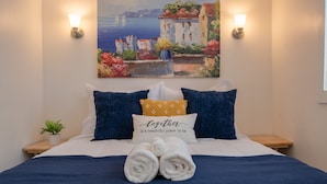 A neatly made bed with rolled towels, two pillows, and a wall-mounted painting.
