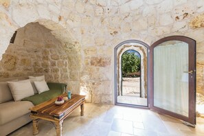 A stone-walled room with a wooden table, a sofa, and a door leading outside. - Villa Irma by BarbarHouse (Carovigno)