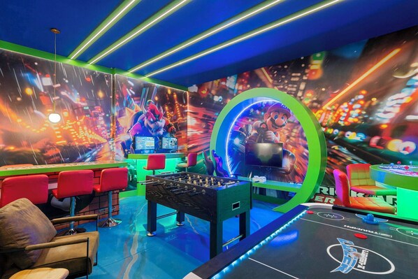 Un espace intérieur lumineux, agrémenté d’un baby-foot, de tabourets de bar rouges et d’un grand écran diffusant des personnages animés.