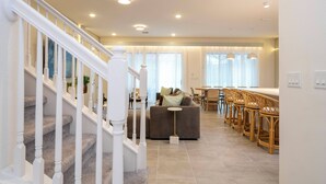 Ein modernes Wohnzimmer mit Treppe, einer Couch und einem Essbereich mit Barhocker.