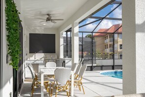Une terrasse ensoleillée avec une piscine, des meubles blancs et une vue sur les bâtiments voisins.