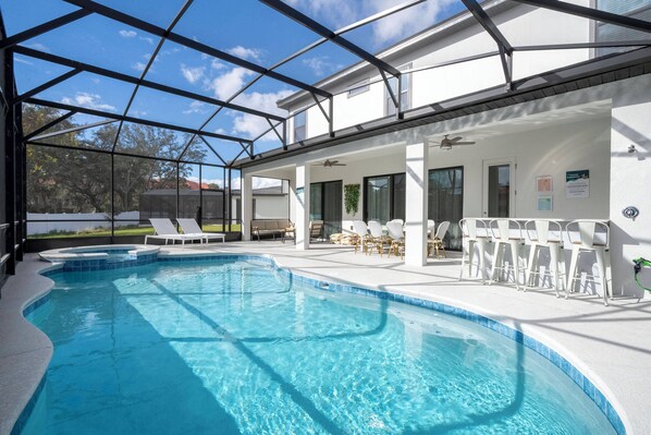 Une piscine entourée de parois en verre, des chaises longues et un patio couvert.