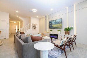 Ein modernes Wohnzimmer mit einem grauen Ecksofa, einem runden Couchtisch, einem flachbildfernseher an der Wand und einem Essbereich mit Holzstühlen und einem Tisch.