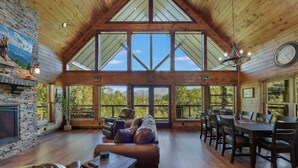 A spacious room with a high ceiling, large windows, a fireplace, a leather sofa, and a dining table.
