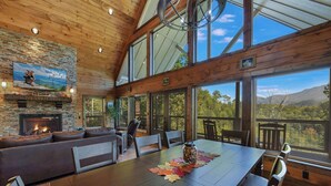 A spacious living area with a fireplace, large windows, and a view of the mountains.
