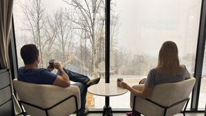 Twee personen zitten aan een klein rond tafeltje in een kamer met grote ramen, uitkijkend op een besneeuwd landschap.