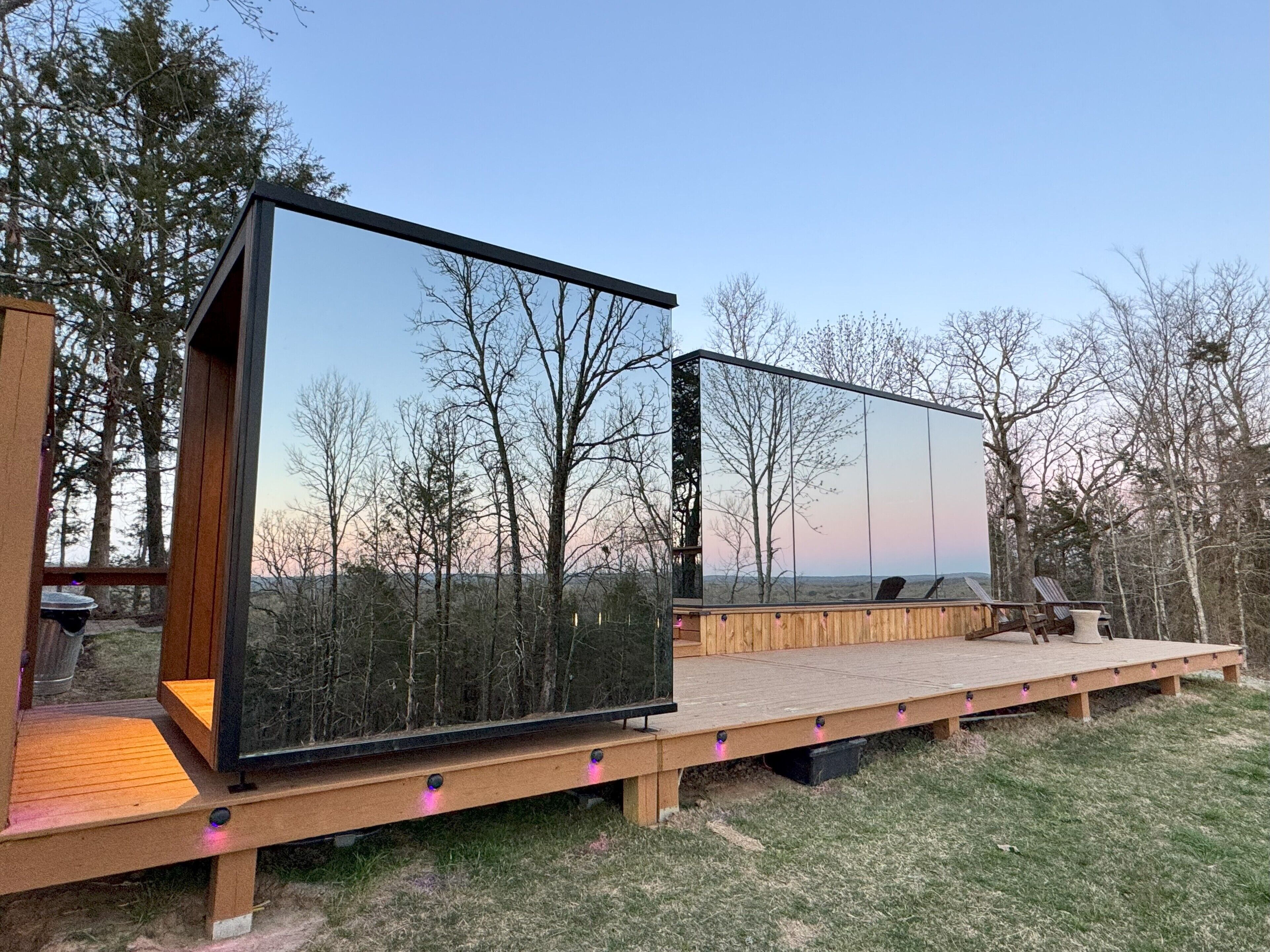 Una terraza moderna al aire libre con una amplia estructura de vidrio reflectante, bancos de madera y vistas del bosque circundante.