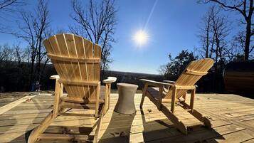 Twee houten Adirondack stoelen op een houten terras, met vrij uitzicht op het landschap en een stralende zon.