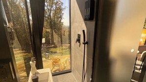 Een moderne badkamer met een douchecabine van glas, een wastafel met zeepdispenser en uitzicht op het groen.