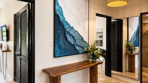 Een gang met een houten console tafel, een groot abstract schilderij en een hanglamp.