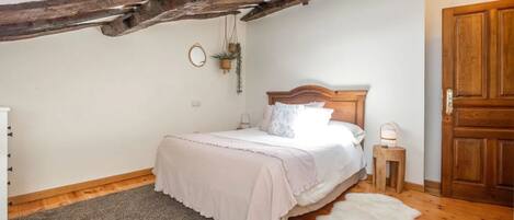 A bedroom with a wooden ceiling, a bed with white bedding, a small bedside table, and a door.