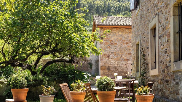 A stone building with terracotta pots on a ledge, wooden furniture, and a tree in the background. - Casa Rural Selmo (Carreno)