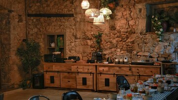 A rustic kitchen with stone walls, wooden cabinets, and hanging light fixtures.