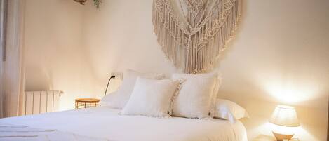 Un dormitorio con cama, dos mesitas de noche, un colgador de macramé y una planta colgante.