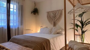A bedroom with a bed, a bench, a hanging plant, and a wooden shelf with towels. - Casa Rural Selmo (Carreno)