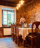 Un comedor con pared de piedra, sillas de madera, una mesa con mantel blanco, un jarrón con flores y un menú.