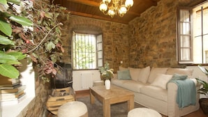 A cozy living room with a stone wall, a wooden coffee table, a sofa, and a fireplace. - Casa Rural Selmo (Carreno)