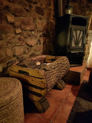 A rustic stone wall, a wooden log fire pit, and a black cabinet with a glass door. - Casa Rural Selmo (Carreno)