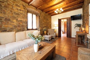 A cozy living room with a stone wall, wooden ceiling, a sofa, a coffee table, and a television. - Casa Rural Selmo (Carreno)