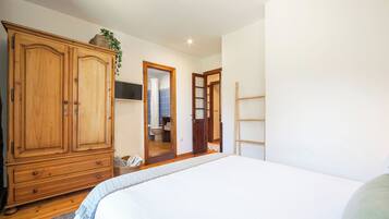 Un dormitorio con un armario grande de madera, una cama con edredón blanco y un baño visible a través de una puerta abierta.