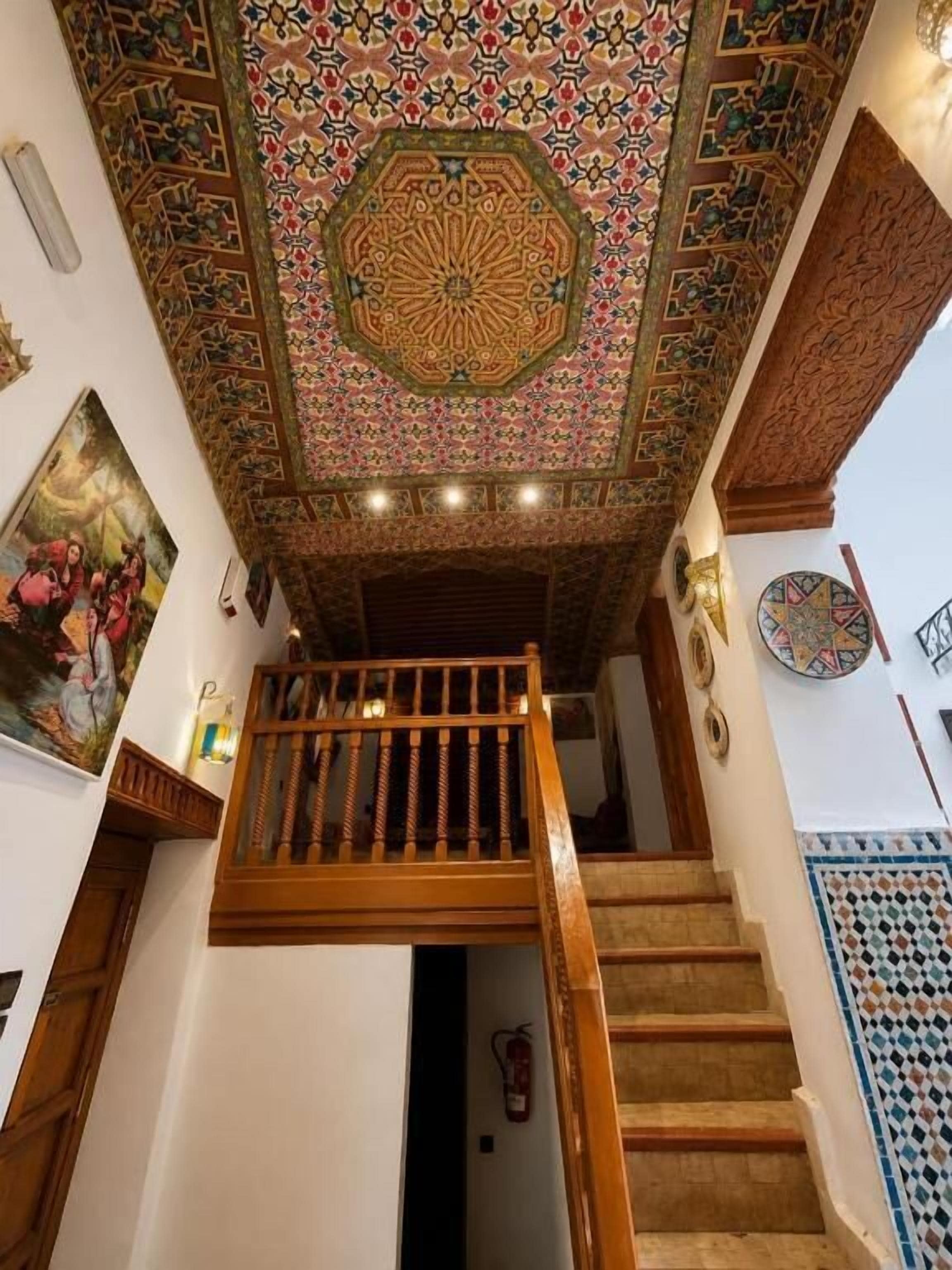 A staircase with a wooden railing, a patterned ceiling, and a wall with a decorative tile border.