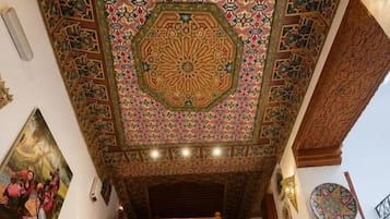 Una escalera con barandilla de madera, techo con diseño y un muro con borde de azulejos decorativos.