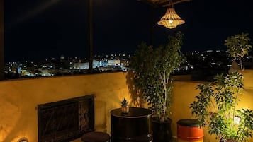 Una terraza en la azotea con lámparas colgantes, plantas en macetas y barriles de colores.