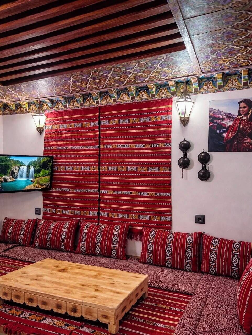 Une pièce avec un canapé à motifs, une table basse en bois, un téléviseur et des appliques murales décoratives.