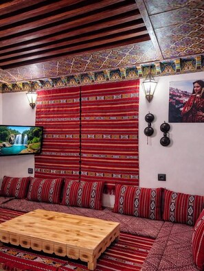 A room with a patterned sofa, a wooden coffee table, a television, and decorative wall lights. - Riad hamad (Fes)