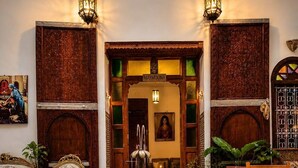 A traditional interior with a fountain, ornate wooden doors, and a seating area with cushions. - Riad hamad (Fes)