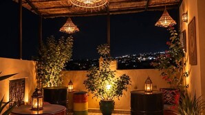 An outdoor seating area with a thatched roof, potted plants, and hanging lanterns. - Riad hamad (Fes)
