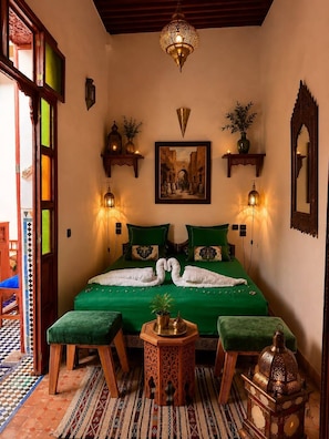 A room with a bed, two wall-mounted lamps, a painting, and a mirror. - Riad hamad (Fes)
