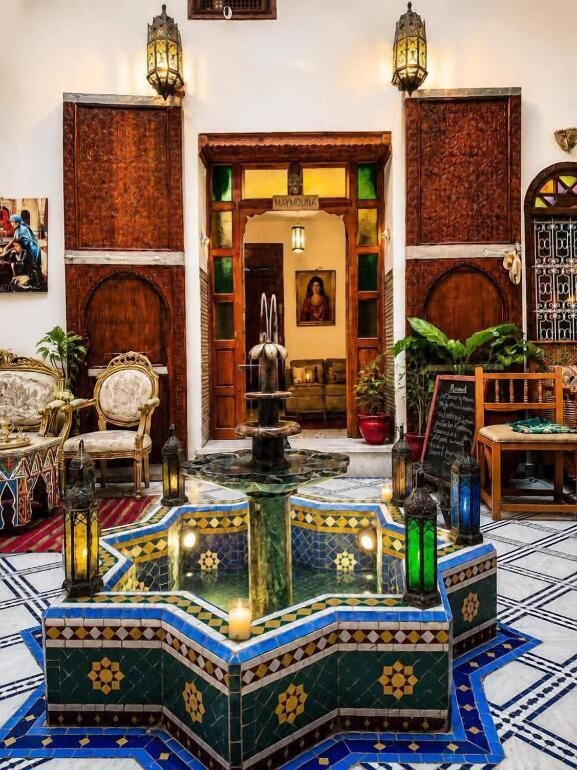 A lobby with a fountain, wooden doors, and a sign reading 'Maymouna'.