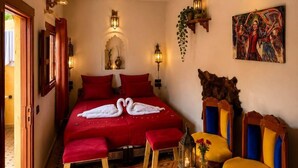 A hotel room with a bed, two chairs, a small table with a vase, and decorative wall sconces. - Riad hamad (Fes)