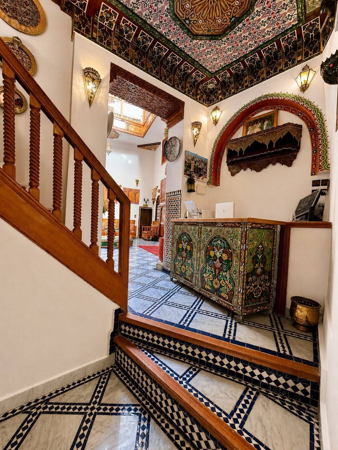 Un escalier orné de motifs complexes en mosaïque mène à une pièce où se trouve un meuble décoratif et des appliques murales.