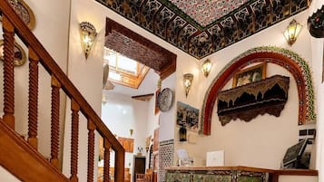 Un escalier orné de motifs complexes en mosaïque mène à une pièce où se trouve un meuble décoratif et des appliques murales.