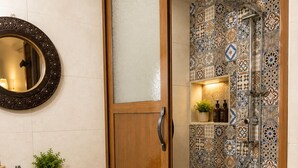 A bathroom with a wooden door, a white sink, a mirror, and a shower with patterned tiles. - Riad hamad (Fes)