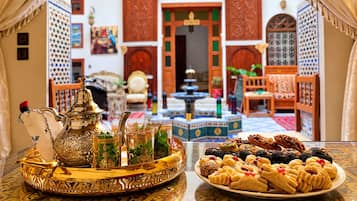 Un décor marocain traditionnel avec une table dressée pour le thé, une fontaine et une variété de pâtisseries.