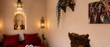 A room with a bed, two wall-mounted lamps, a painting, and a small table with a plant.